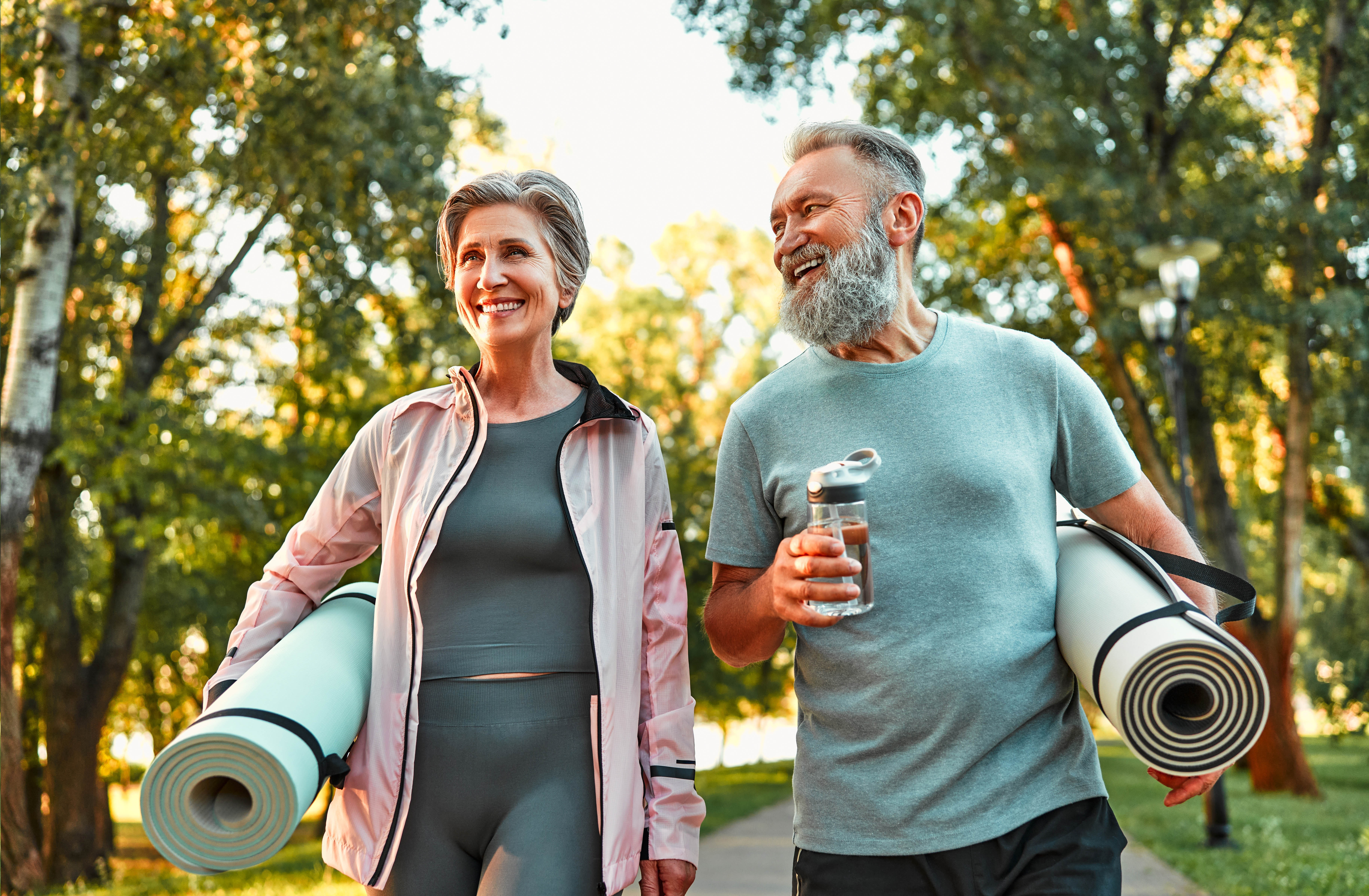 Older couple walking outside with their yoga mats rolled up under their arms Older couple walking outside with their yoga mats rolled up under their arms